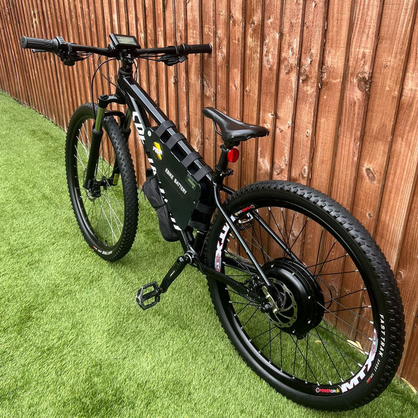 Black electric bike on green grass with a wooden fence in the background