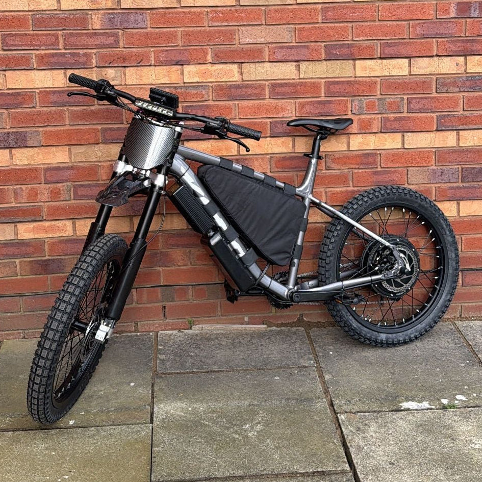 Black bicycle leaning against a brick wall on a pavement.